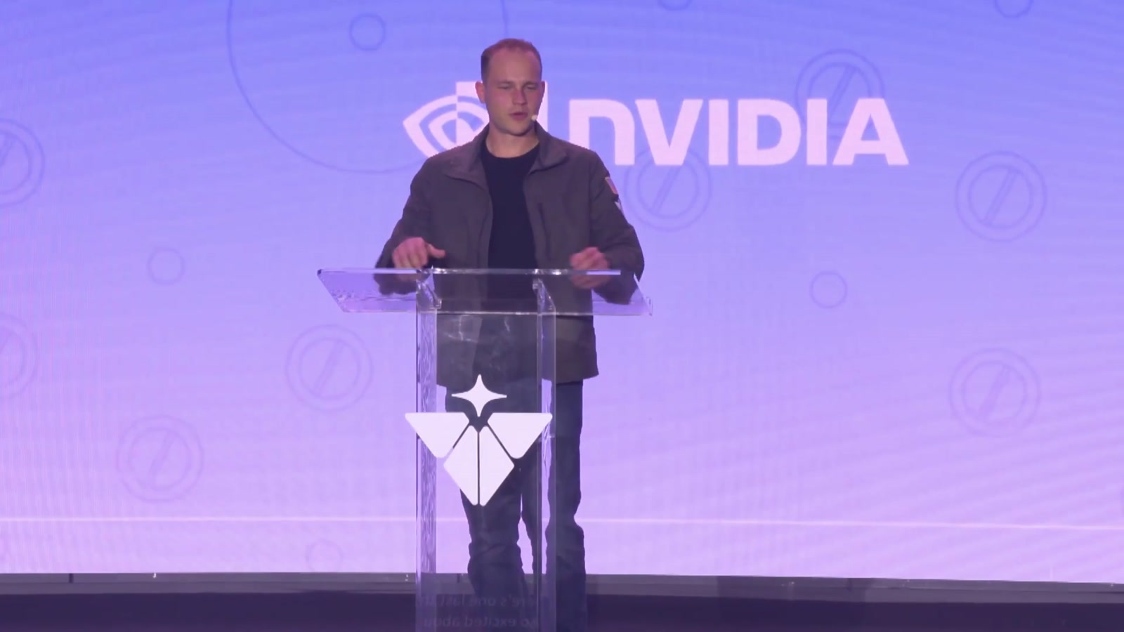 Der Gründer von Valar Atomics steht an einem gläsernen Rednerpult, im Hintergrund eine große Leinwand mit dem NVIDIA-Logo und dem rautenförmigen Logo von Valar Atomics.