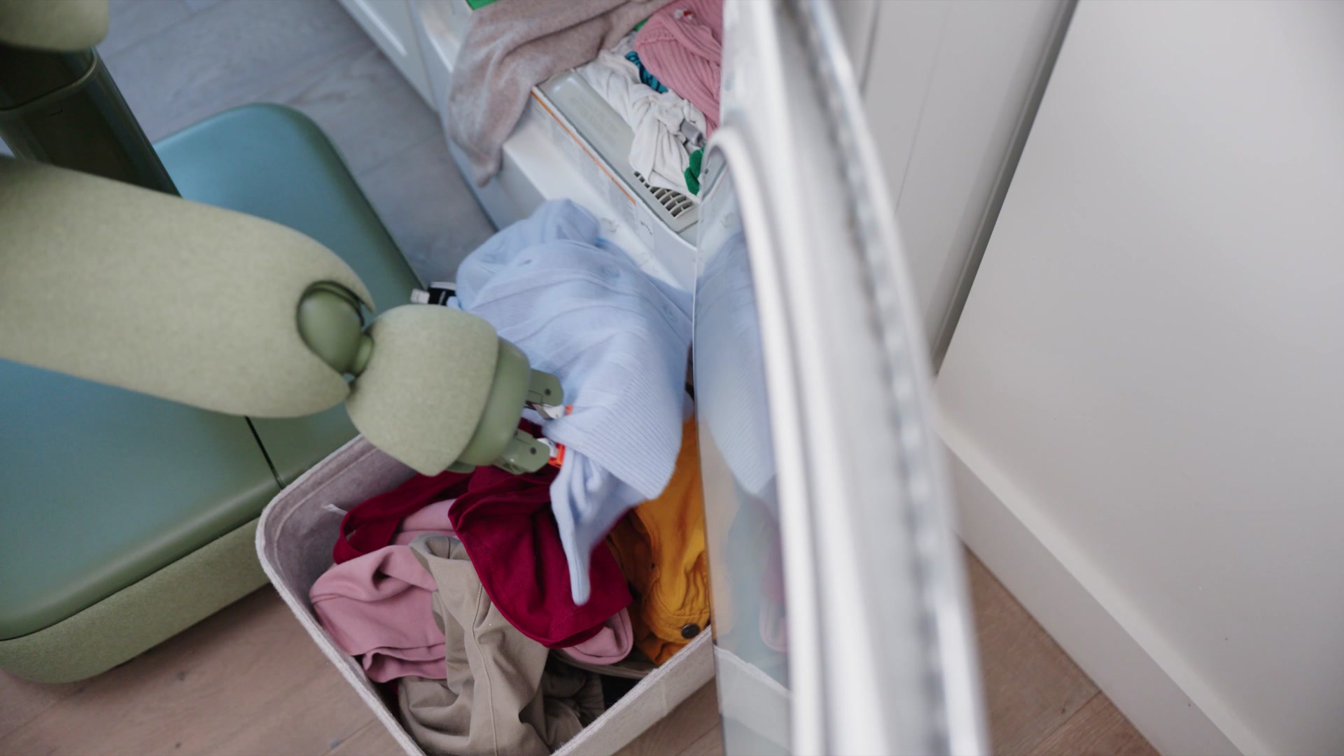 Isaacs Greifer hebt bunte Kleidung aus einem Wäschekorb, im Vordergrund die runde Öffnung einer Waschmaschine